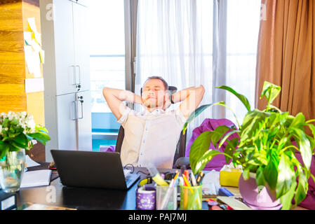 Satisfaits de travailler. Prendre le temps d'une minutes de pause. Cheerful young man holding hands behind head et garder les yeux clos tandis qu'assis à son wo Banque D'Images