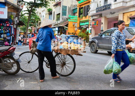 Une femme portant son vélo à Hanoi, Vietnam, portant un chapeau conique traditionnel. Les femmes vendent des produits sur leurs bicyclettes sont un site commun à Hanoi Banque D'Images