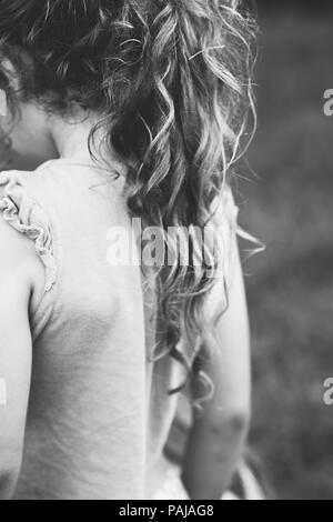 Le noir et blanc portrait de petite fille à l'extérieur avec de longs cheveux bouclés, vue de dos. L'accent doux Banque D'Images