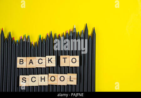 Retour à l'école recueillies auprès d'éléments en bois lettre bloc sur tas de crayons de couleur noir sur fond jaune Banque D'Images