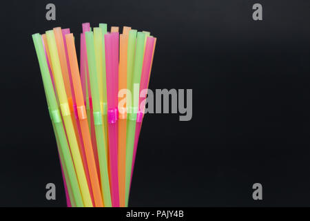 Libre à usage unique très colorés de paille en plastique jetables grappe cocktail de couleur vive fun party concept isolé sur fond noir Banque D'Images