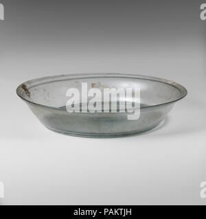Plat en verre. Culture : Roman, chypriote. Dimensions : 1 3/4 x 8 3/16 in. (4,5 x 20,9 cm). Date : 1er siècle de notre ère. Bleu pâle translucide vert. Le torchage, arrondies, avec jante extérieur horizontal rib ci-dessous ; un peu côté convexe de hauteur inégale, effilé vers le bas à large, intregral anneau de base tubulaire ; fond plat mais avec kick au centre, formant dôme épaissi, et des traces de pontil cicatrice. Intact ; bulles piqûre et le soufflage de stries ; certains ternissement et légère, l'iridescence avec de petites parcelles d'altération à la crème. Musée : Metropolitan Museum of Art, New York, USA. Banque D'Images