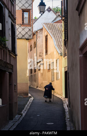 Une vieille dame lutte jusqu'à la rue dans le village pittoresque de Ribeauvillé, France Banque D'Images