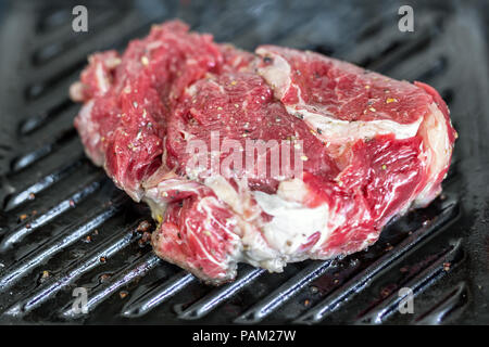 Close-up matières bifteck de faux-filet frais savoureux sur le gril poêle en fonte. La viande de bœuf biologique assaisonné de poivre du moulin cuisson sur barbecue. Banque D'Images