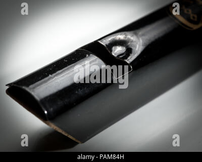 Détails d'une tin whistle noir posé sur une surface réfléchissante blanche Banque D'Images