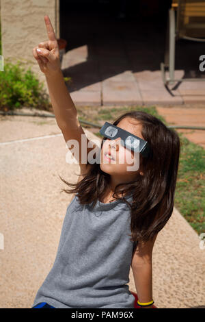 Une jeune fille, avec les cheveux bruns, est assis sur une boule à l'extérieur sur une journée ensoleillée. Elle porte des lunettes, verres papier Eclipse solaire avec des filtres pour le Banque D'Images