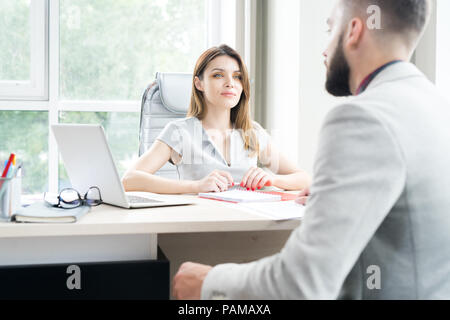 Portrait of beautiful businesswoman sitting at desk in office grand et parler aux client Banque D'Images