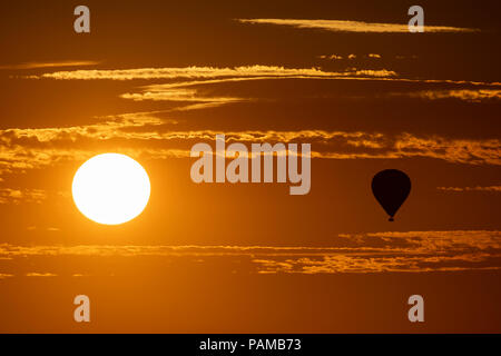 Une montgolfière flotte au-dessus de la campagne du Wiltshire au coucher du soleil sur la journée la plus chaude de l'année au Royaume-Uni. Banque D'Images