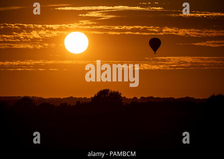 Une montgolfière flotte au-dessus de la campagne du Wiltshire au coucher du soleil sur la journée la plus chaude de l'année au Royaume-Uni. Banque D'Images