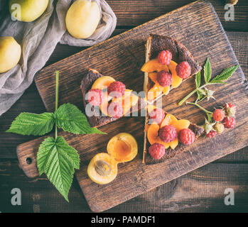 Morceaux de Tarte au fromage cottage avec des fraises et d'abricots sur une planche de bois brun, vue du dessus Banque D'Images