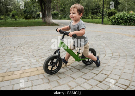 Happy boy riding un petit vélo dans le parc Banque D'Images