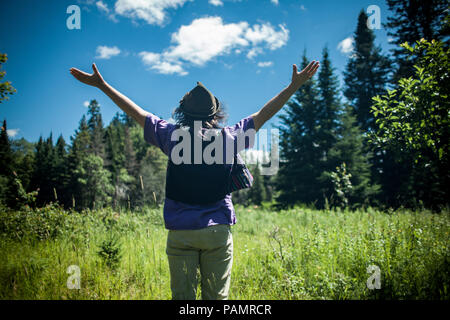 Homme portant un chapeau avec ses bras en profitant d'une belle journée ensoleillée dans la nature, vu de derrière Banque D'Images