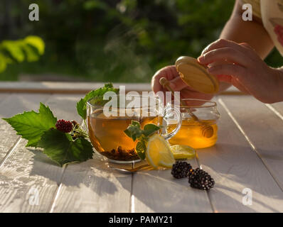 Durée de vie lente. Concept de petit déjeuner sain. Tasse de thé aromatique, baies et miel sur une table en bois blanc dans le jardin Banque D'Images