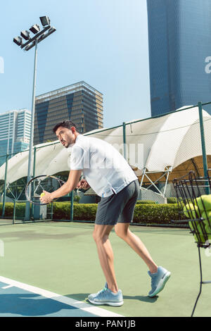 Jeune homme jouant au tennis à l'extérieur, dans un quartier moderne de la ville Banque D'Images