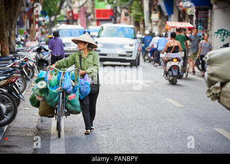 Une femme portant son vélo à Hanoi, Vietnam, portant un chapeau conique traditionnel. Les femmes vendent des produits sur leurs bicyclettes sont un site commun à Hanoi Banque D'Images