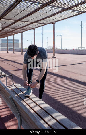 L'homme sportif ses chaussures laçage sur un banc sous roofing Banque D'Images