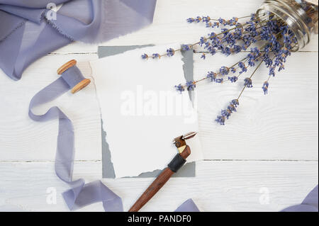Carte vierge blanc ribbon bow sur fond de tissu bleu et rose avec des fleurs de lavande et Plume calligraphique sur un fond blanc. Immersive avec enveloppe et carte vierge. Mise à plat. Vue d'en haut Banque D'Images