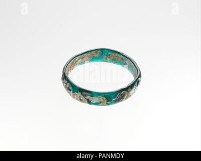 Bracelet en verre avec décoration impressionné. Culture : Roman. Dimensions : hors tout : 1/4 x 2 3/4 in. (0,6 x 7cm). Date : fin 4ème-5ème siècle de notre ère. Bleu turquoise translucide. Bande circulaire à bords arrondis et côtés légèrement inégale ; dans la section convexe avec télévision côté intérieur ; pas de joints apparents. Surface extérieure ornée d'une série de treize estampillé cercles, chacun représentant un lion faisant face à droite, la bouche ouverte, grande crinière et queue relevée au-dessus de son dos. Intacte, à l'exception d'une puce altérés sur le bord intérieur ; de nombreuses bulles allongée et piqûre ; dulling, quelques piqûres profondes, s'évanouir, et correctifs irisation Banque D'Images