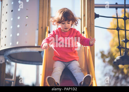 Portrait de petite fille assise sur la diapositive à l'aire de jeux Banque D'Images