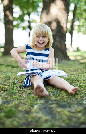 Portrait of laughing little Girl with painted face sitting sur le sol dans la nature Banque D'Images