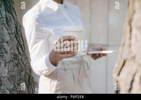 Young businesswoman transportant tasse de café et d'un smartphone Banque D'Images