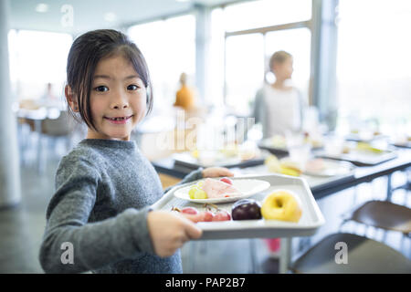 Portrait of smiling schoolgirl carrying tray en cantine scolaire Banque D'Images