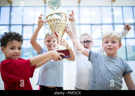 Les élèves heureux holding trophy in gym Banque D'Images