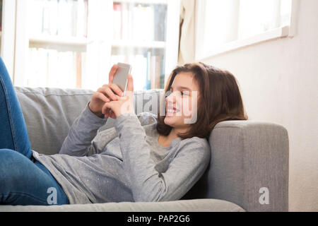Smiling girl lying on couch at home using cell phone Banque D'Images