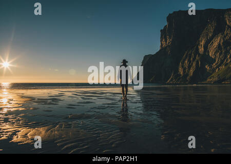 La Norvège, les îles Lofoten, Moskenesoy, homme qui marche dans le coucher du soleil à Kvalvika Beach Banque D'Images