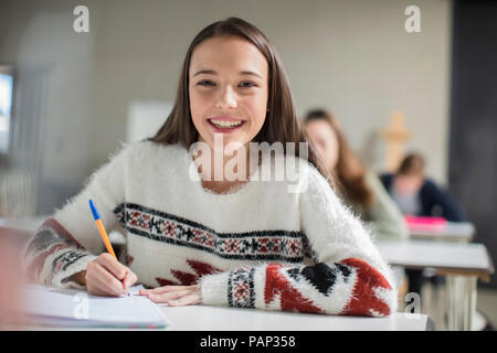 Portrait of smiling teenage girl écrit dans un livre d'exercices en classe Banque D'Images
