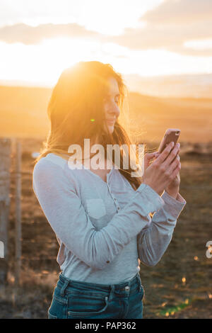 L'Islande, woman using smartphone au coucher du soleil Banque D'Images