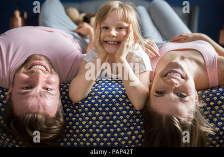 Cheeky little girl lying on bed with parents Banque D'Images