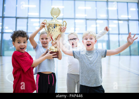 Les élèves heureux holding trophy in gym Banque D'Images