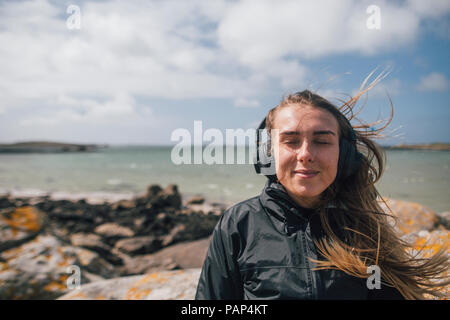 France, Bretagne, Landeda, jeune femme portant des écouteurs à la côte Banque D'Images