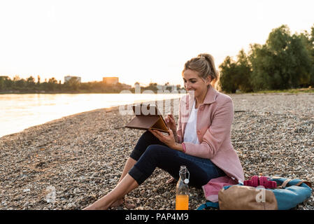 Young blonde woman using tablet sur Riverside dans la soirée Banque D'Images