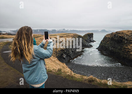 Vue arrière de l'Islande, young woman taking picture with smartphone at coast Banque D'Images