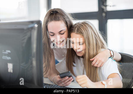 Smiling teenage girls using cell phones in computer class Banque D'Images
