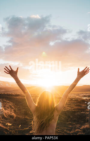 L'Islande, jeune femme aux bras levés au coucher du soleil Banque D'Images