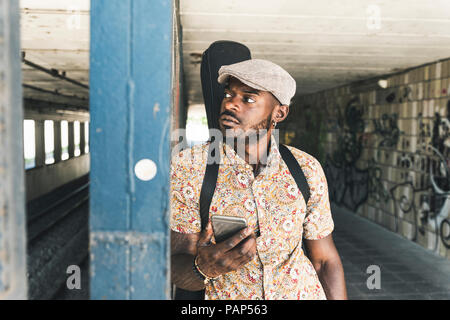 Jeune homme de la ville, transportant des cas, l'utilisation de guitare smartphone Blackberry Banque D'Images