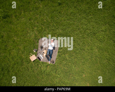 Bird's Eye View of woman lying on blanket sur prairie avec chien à l'aide de tablet Banque D'Images
