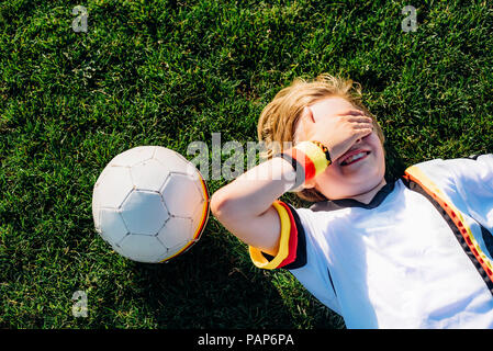 Garçon en allemand soccer shirt lying on grass, couvrant les yeux Banque D'Images