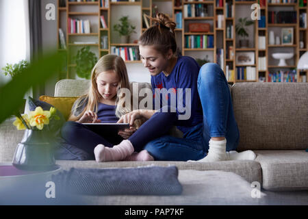 Deux soeurs assis sur le canapé, jouant avec digital tablet Banque D'Images