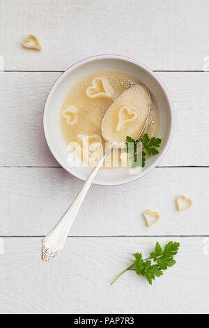 Cuillère en argent dans un bol de soupe au poulet avec des nouilles en forme de cœur et le persil Banque D'Images