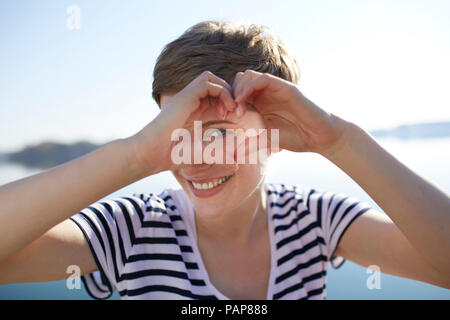 Portrait of smiling woman in front of lake coeur en forme avec ses doigts Banque D'Images