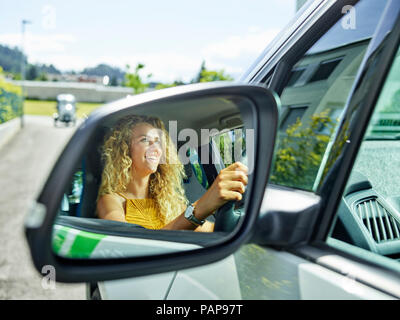Reflet dans wing mirror of smiling woman driving voiture électrique Banque D'Images