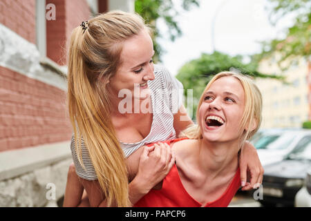 Happy young woman giving ami piggyback ride dans la ville Banque D'Images