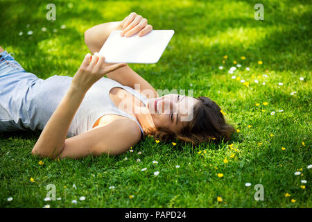 Young woman lying on meadow, à l'aide de tablet Banque D'Images