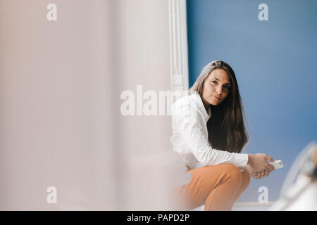 Young businesswoman sitting at fenêtre, using smartphone Banque D'Images