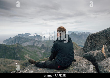 La Norvège, les îles Lofoten, Moskenesoy, jeune homme assis à Hermannsdalstinden Kjerkefjord, à plus de Banque D'Images