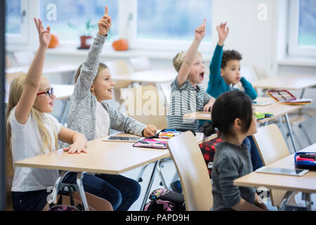 Heureux les élèves lèvent la main dans la classe Banque D'Images